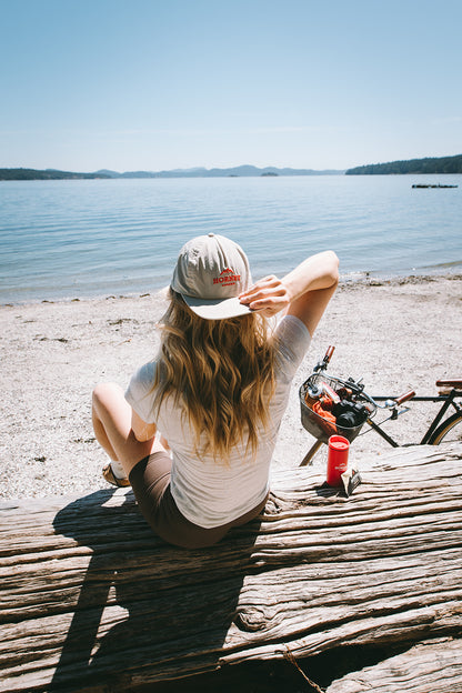 Woman sitting on a beach log wearing hornby organic hat backwards
